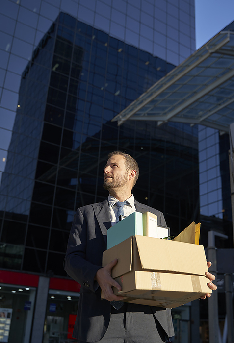 Businessman with office belongings standing in front of office building