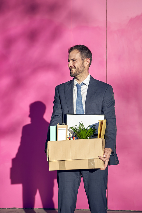 Smiling businessman with box in front of wall