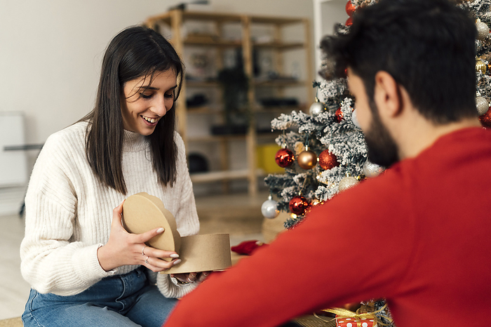 Smiling woman opening gift in front of boyfriend at home Smiling woman opening gift in front of boyfriend at home
