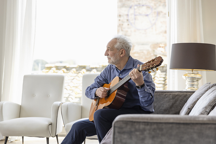 Senior man playing classical guitar on sofa in bright modern living room  Florence, Italy Senior man playing guitar sitting on sofa in living room at home