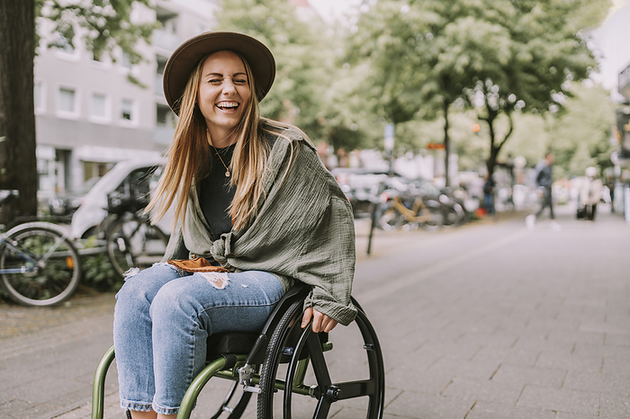 Cheerful young woman sitting in wheelchair at sidewalk