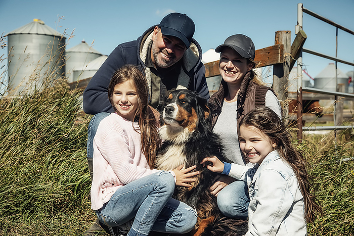 Family portrait of parents with their two young girls posing with the family dog  on their farm; Alcomdale, Alberta, Canada, Photo by LJM Photo / Design Pics