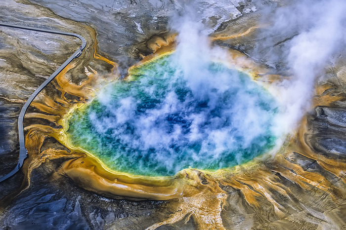 Grand Prismatic Spring is one of the largest and most beautiful examples of a common hydrothermal feature in Yellowstone National Park and one of the largest hot springs in the United States. The prismatic or colorful features come from several sources; the deep blue in the center is the clear super-heated water circulating up from the subterranean heat source and as the water cools at the edges of the pool and on the sinter terraces, bacteria and algae produce the rainbow of colors. This hot spring was specifically mentioned in Osborne Russell's Journal of a Trapper, by the name of Boiling Lake, which apparently was a name given to it by Rocky Mountain fur trappers in the 1830s, in Yellowstone National Park; Wyoming, United States of America, Photo by Tom Murphy / Design Pics