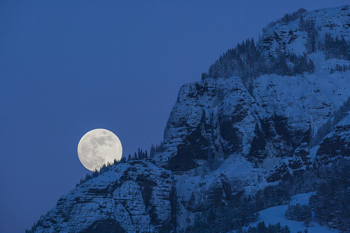 Full Moon rising in a blue, night sky behind a mountain cliff in Lamar Valley in Yellowstone National Park; Wyoming, United States of America, Photo by Tom Murphy / Design Pics