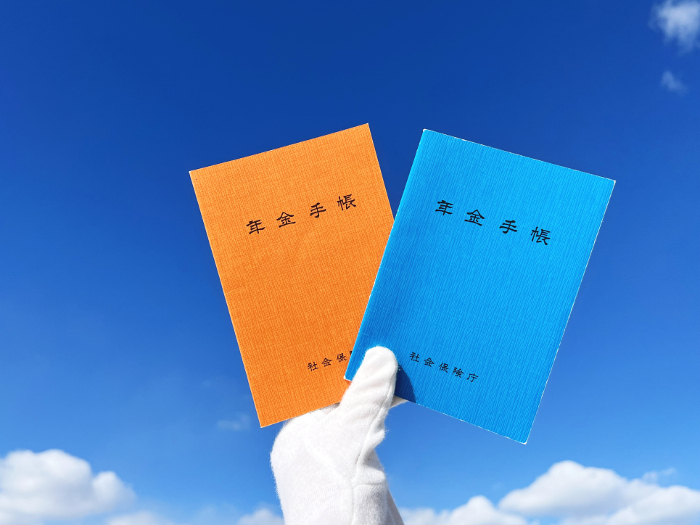 Orange and blue pension book held with white gloves_blue sky background