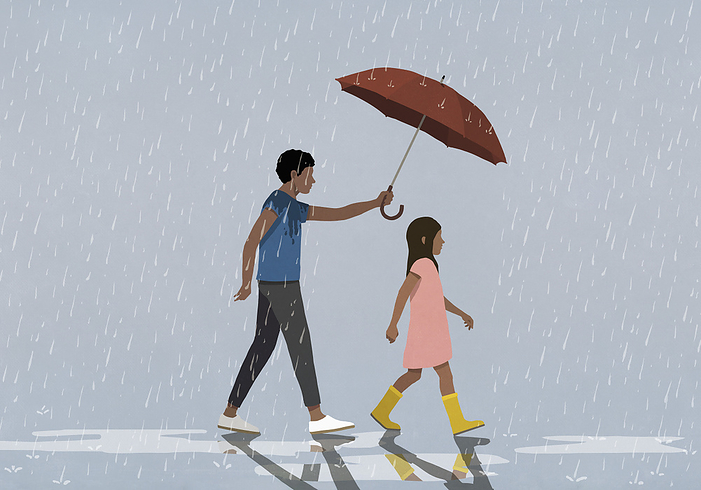 Father holding umbrella over daughter walking in rain