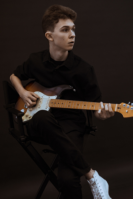 A young boy in the black clothes plays guitar
