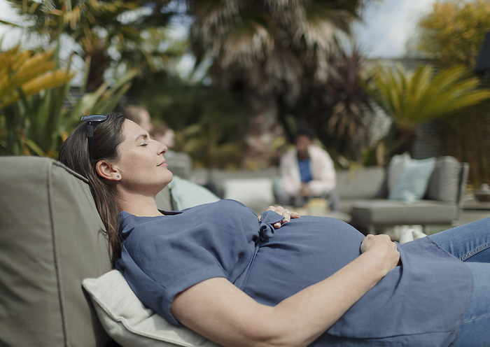 Serene pregnant woman relaxing on sunny patio lounge chair