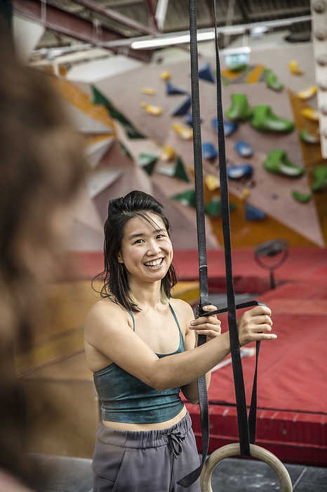 Smiling woman exercising at gymnastics rings in climbing gym