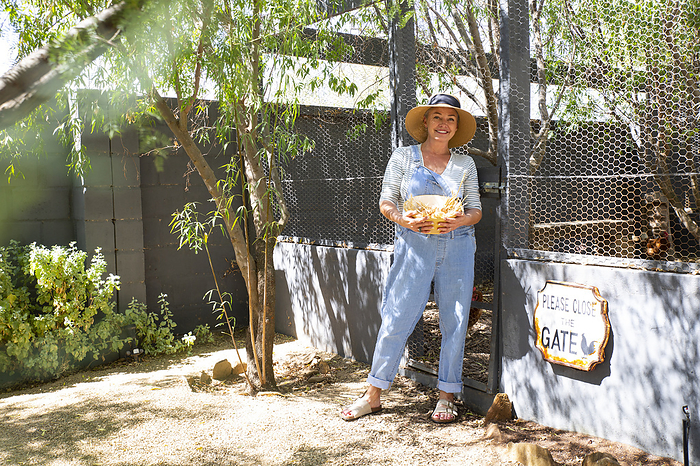 Smiling farm owner wearing hat holding bowl at entrance on sunny day