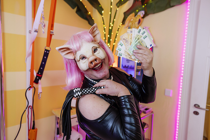 Happy transvestite man wearing pig mask holding whip and paper currency