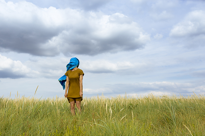Woman covering face with blue scarf standing at meadow