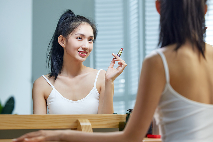 A beautiful young woman lipstick herself in the mirror