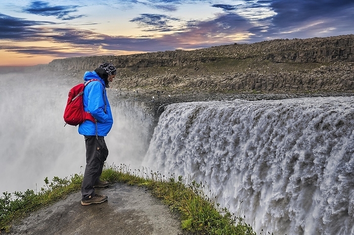 Hiker at the edge of Dettifoss, tourist looking down into the gorge, waterfall with falling masses of water, river J枚kuls谩 Fj枚llum, evening sky, North Iceland, Iceland, Europe