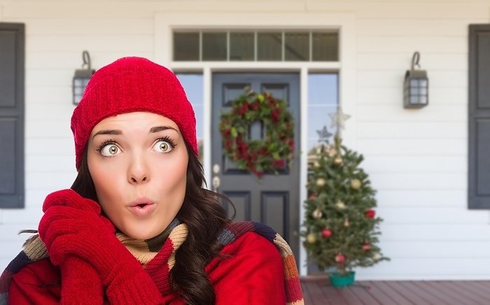 Young girl wearing scarf, red cap and mittens standing on christmas decorated front porch