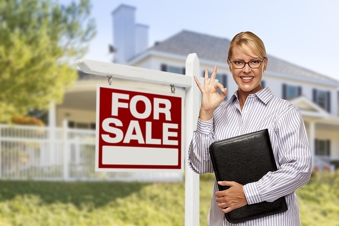 Female real estate agent in front of home for sale sign and house