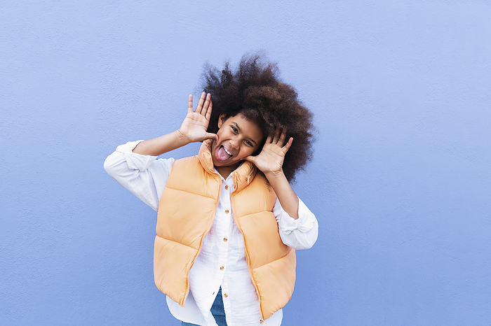 Girl with Afro hairstyle sticking out tongue standing against blue background