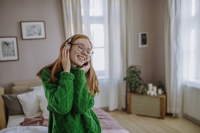 Happy woman with eyes closed enjoying music through wireless headphones at home