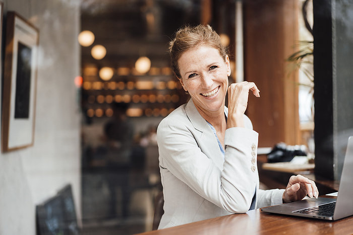 Happy businesswoman with laptop sitting in cafe