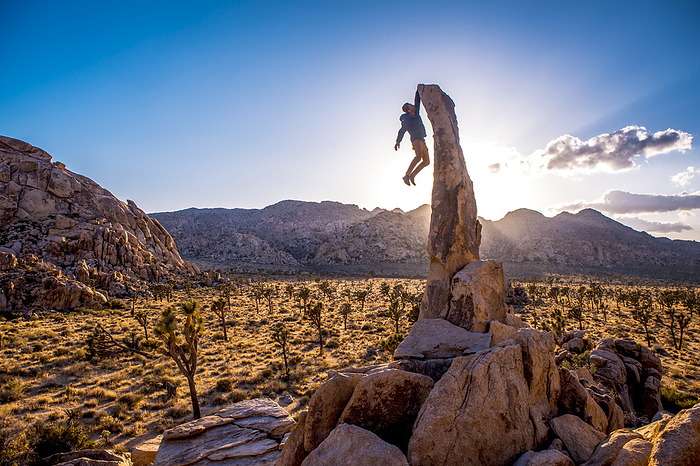 The Aguille de Joshua Tree stands above the desert at sunset as a man boulders to the top., Photo by Ben Horton / Design Pics