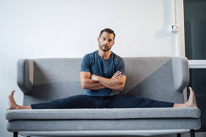 Man stretching legs sitting with arms crossed on sofa at home