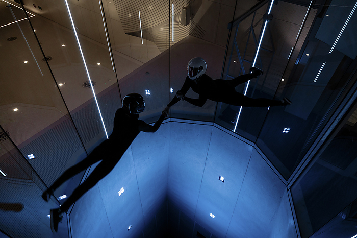 Athletes holding each others hands flying in illuminated wind tunnel