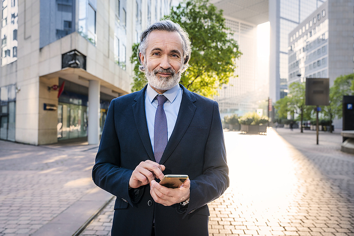 Smiling businessman with smart phone standing in office park