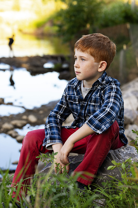 Outdoor portrait of a boy with red hair sitting beside a creek; Edmonton, Alberta, Canada, Photo by LJM Photo / Design Pics