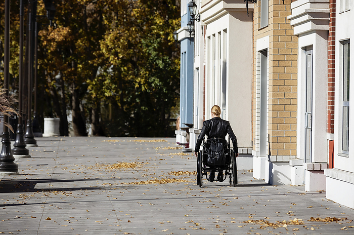 Young paraplegic woman in her wheelchair going down a city walkway on a beautiful fall day; Edmonton, Alberta, Canada, Photo by LJM Photo / Design Pics