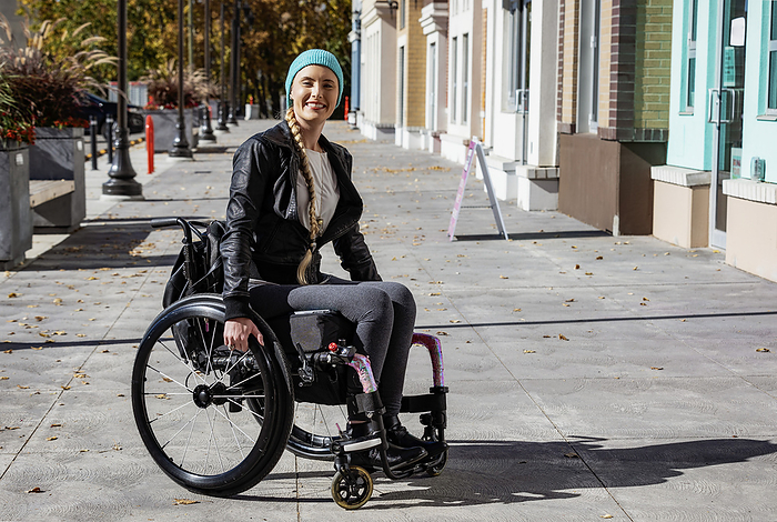 Young paraplegic woman in her wheelchair on a city walkway on a beautiful fall day; Edmonton, Alberta, Canada, Photo by LJM Photo / Design Pics