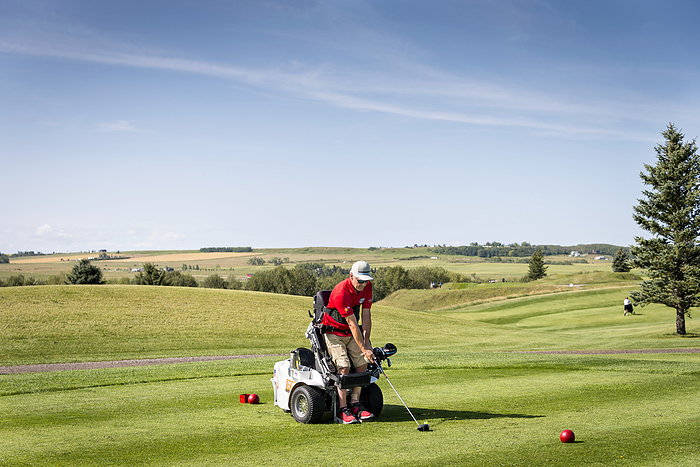 Disabled golfer using a specialized golf assistance motorized hydraulic wheelchair; Okotoks, Alberta, Canada, Photo by Brad Callihoo / Design Pics