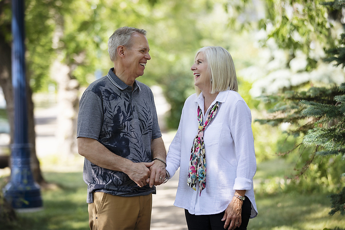 Mature couple holding hands and sharing a moment together in laughter while walking outdoors on a park trail; Edmonton, Alberta, Canada, Photo by LJM Photo / Design Pics