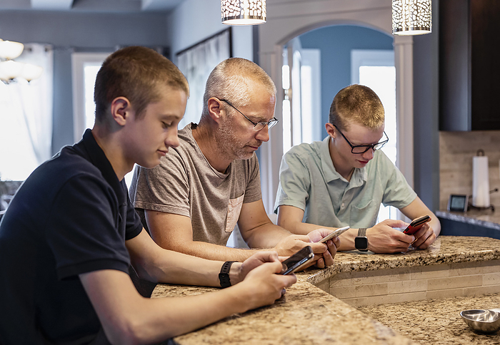 Father and two sons sit at the kitchen island at home using their smart phones; Edmonton, Alberta, Canada, Photo by LJM Photo / Design Pics