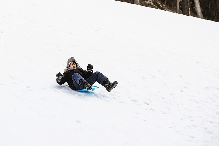 Young Boy Riding Down A Snowy Hill On A Blue Plastic Sled At A Mountain Resort; Fairmont Hot Springs, British Columbia, Canada, Photo by LJM Photo / Design Pics