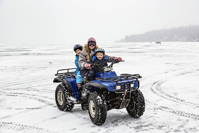 A Mother And Two Young Sons Riding An ATV On A Frozen Lake And Posing For The Camera; Invermere, British Columbia, Canada, Photo by LJM Photo / Design Pics