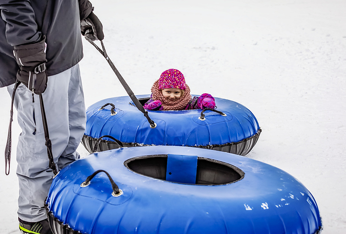 A father and his young daughter getting ready to go tubing down a ski hill together; Fairmont Hot Springs, British Columbia, Canada, Photo by LJM Photo / Design Pics