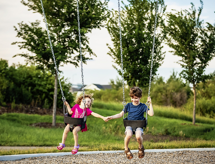 Young girl and boy holding hands while playing on a swing set at a playground; St. Albert, Alberta, Canada, Photo by LJM Photo / Design Pics