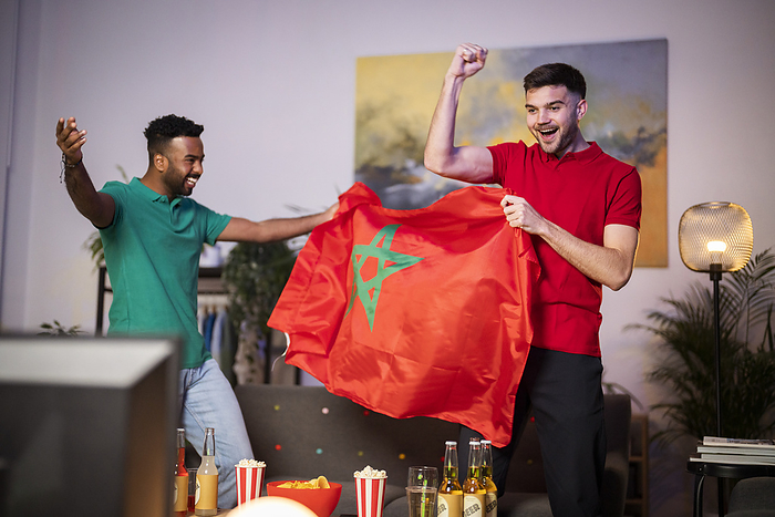 Happy football fans with Moroccan flag cheering at home