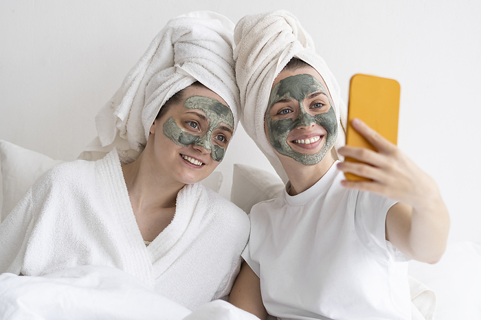 Self care day Happy friends wearing facial masks taking selfie through smart phone