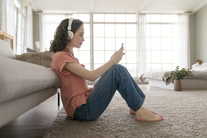 Young woman using smart phone sitting on carpet at home
