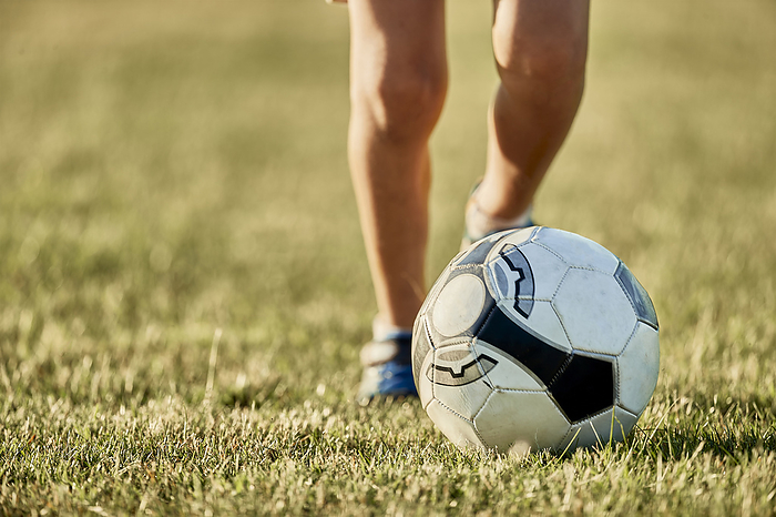 Legs of boy in front of soccer ball at sports field