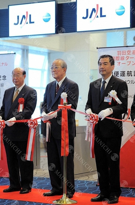 Japan Airlines President Ken Ohnishi and Chairman Kazuo Inamori at the ribbon cutting ceremony for the opening of Haneda Airport s new international terminal. At the newly opened international terminal, JAL President Ken Onishi, JAL Chairman Kazuo Inamori, and Ota Ward Mayor Tadayoshi Matsubara  from right  cut the ribbon to celebrate the first flight departure at Haneda Airport on October 21, 2010 at 7:56 a.m. Photo by Koichiro Tezuka