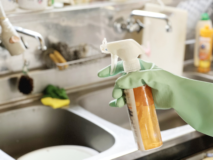 Hands holding detergent with plastic gloves cleaning the kitchen