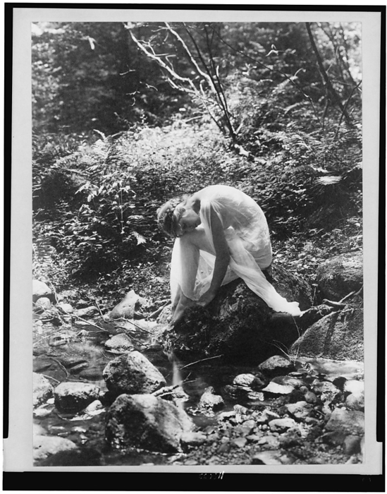 Wood nymph, between 1900 and 1915. Creator: Frances Benjamin Johnston. Wood nymph, between 1900 and 1915. Woman in classical drapery seated on rock near stream in woods.