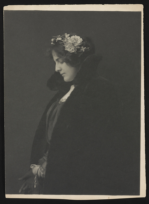 Miss Ethel Reed,  1896  . Creator: Frances Benjamin Johnston. Miss Ethel Reed,  1896  . Photograph shows poster artist Ethel Reed, three quarter length portrait, left profile, looking down, possibly pulling on gloves, wearing an overcoat or cape and a hat with floral arrangement.