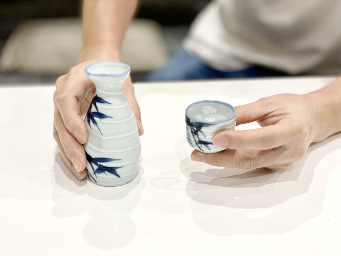 A man holding a sake bottle and a cup filled to the brim with sake