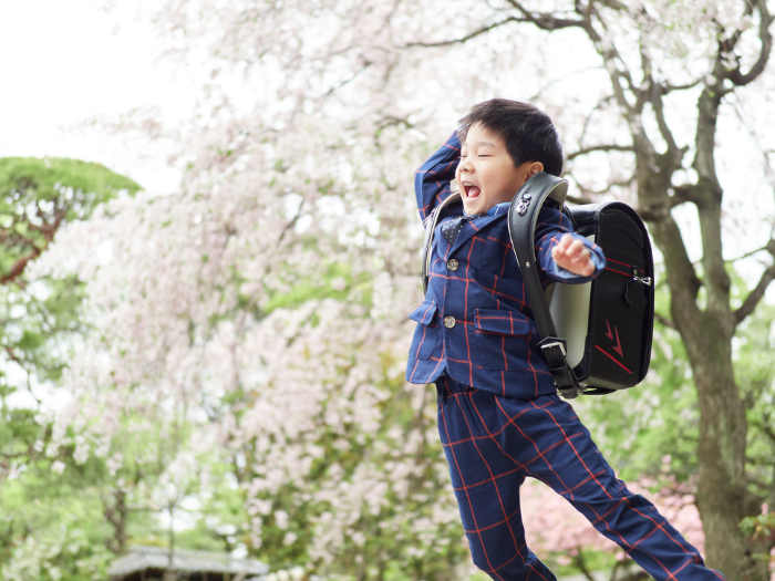 New first-year students jumping with their school bags on their backs against a background of cherry trees.