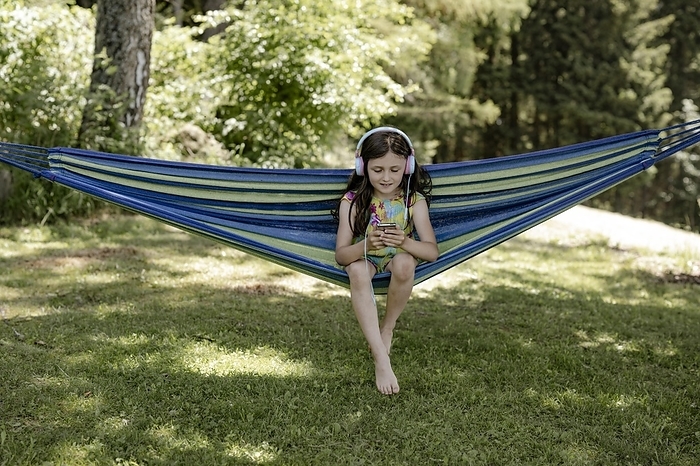 Girl, 8 years, sitting in a hammock in the shade and listening to music with headphones, Photo by Michaela Begsteiger