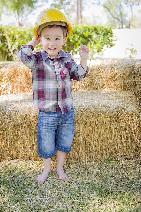 Cute young mixed-race boy laughing with hard hat outside near hay bale, Photo by Andy Dean