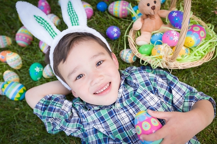 mixed-race chinese and caucasian boy outside wearing rabbit ears playing with easter eggs, Photo by Andy Dean